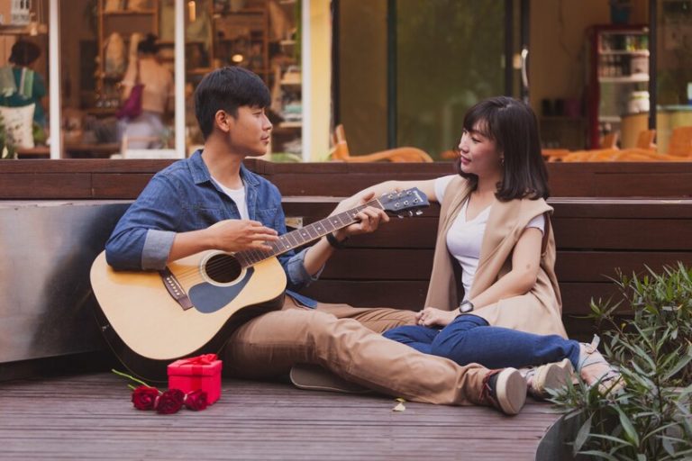 man-playing-guitar-while-looking-his-girlfriend-with-gift-flower_23-2147592886